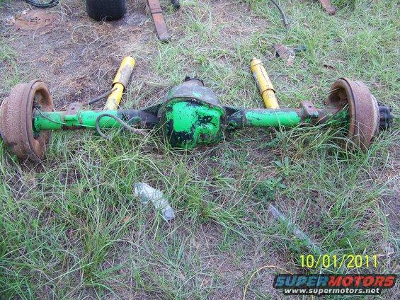 Green Dana 60 axle with yellow shocks and rusty brake drums on grassy ground
