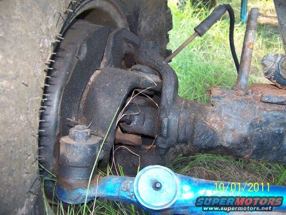Close-up of a vehicle's front axle and steering linkage, showing the tie rod and ball joint. A tire is visible on the left