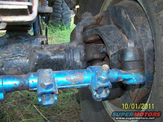 Close-up of rusty blue tie rod and black steering knuckle with a tire in the background