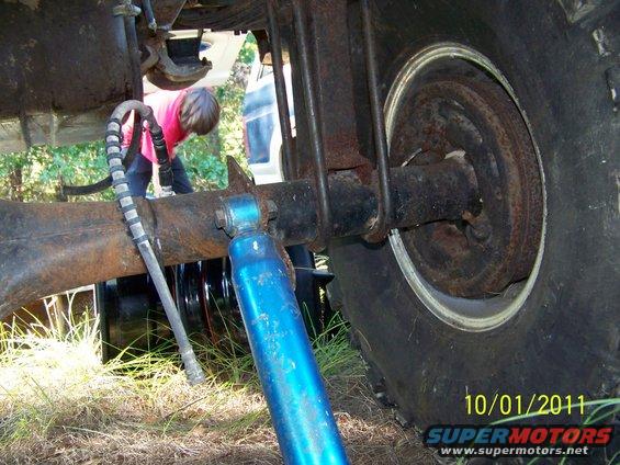 Rear axle assembly with blue shock absorber and U-bolts, tire visible