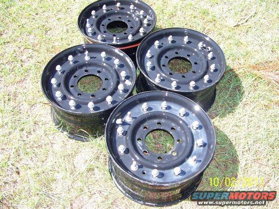four black steel wheels with lug nuts on grass