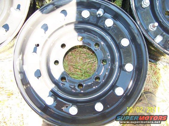 two black truck wheels with silver lug nuts, one wheel is half painted white