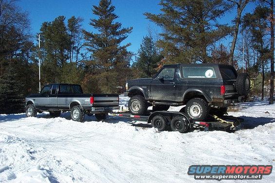 1995 Ford F-250 towing a lifted Ford Bronco on a trailer in the snow
