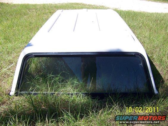 White truck topper with a tinted window lying on grass