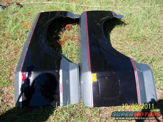 Two black and gray vehicle fenders with red pinstriping, lying on grass