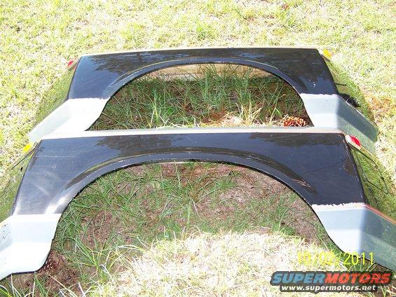 Two black vehicle fenders with gray trim laid on grass