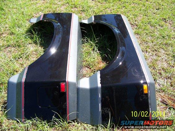 Two black fenders with grey and red stripe accents, one with a red reflector, the other with an amber marker light