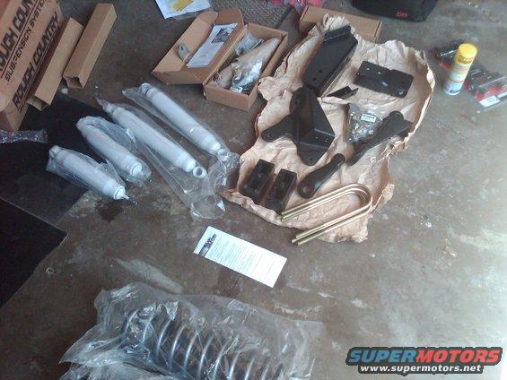 Lift kit components including shocks, U-bolts, and brackets laid out on a concrete floor