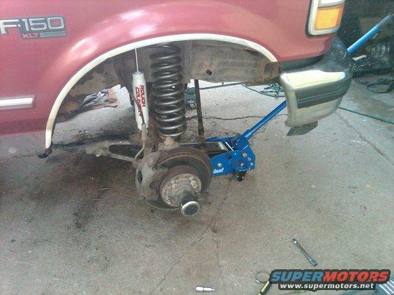 Red 1992 Ford F-150 XLT with front wheel removed, jack supporting suspension