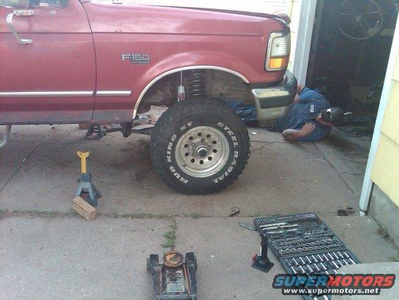 1992 Ford F-150 truck with large tires, jack stands, and a mechanic working underneath