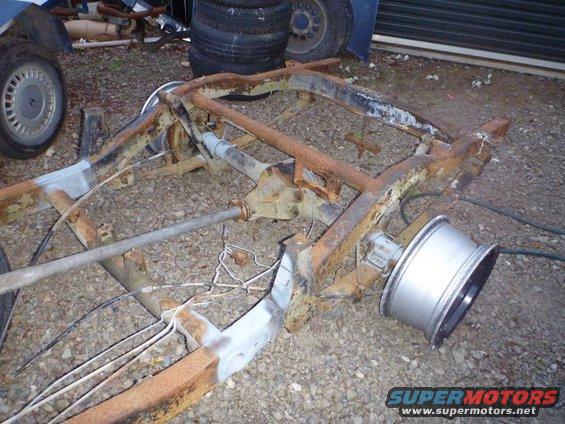 rusted vehicle frame with rear axle and suspension parts, one wheel attached