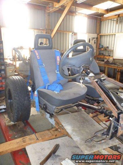 Custom vehicle chassis with racing seats, blue harnesses, and steering wheel