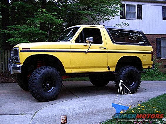 Yellow lifted Ford Bronco parked on a driveway, side view