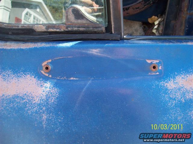 Blue truck door with two circular holes where a handle was removed. Rust and peeling paint are visible