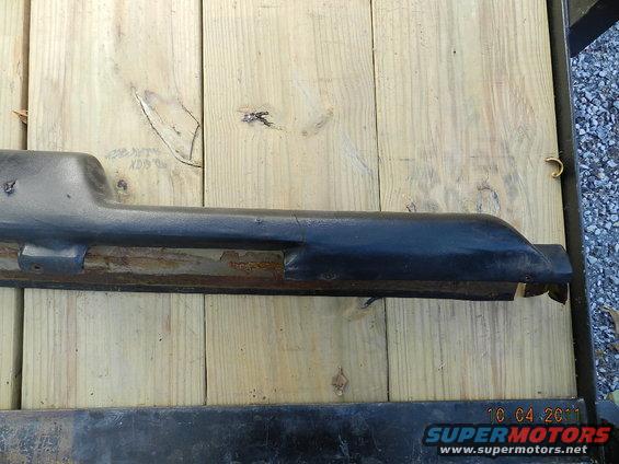 Black plastic trim piece with visible rust underneath, resting on wooden planks