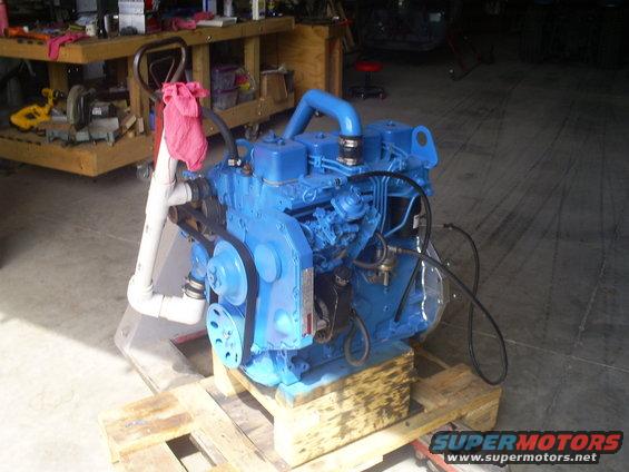blue engine on wooden pallet, some pipes and hoses attached