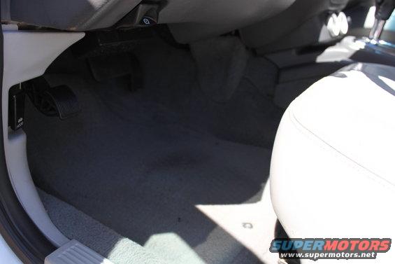 driver's side floor area with pedals and part of a white seat