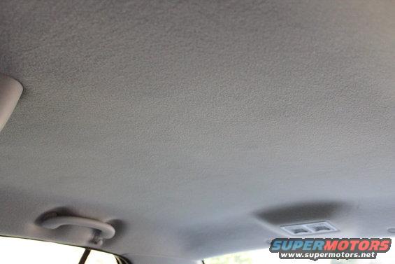 Gray car interior ceiling with a grab handle and a light fixture. Watermark "SUPERMOTORS www.supermotors.net" is visible