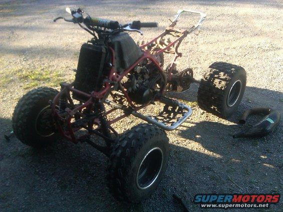 ATV frame with engine, radiator, handlebars, and wheels. Exhaust pipe is detached