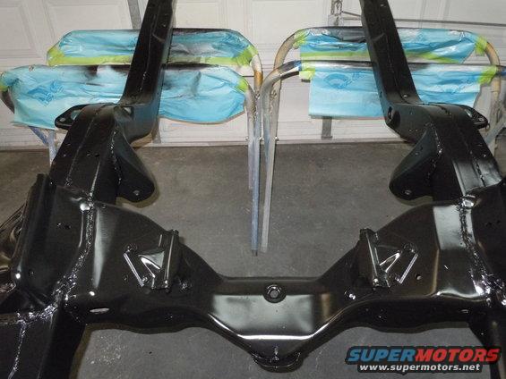 Black painted car frame sections on a stand, covered with blue and green masking tape