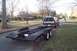 1992 Ford F-150 - A 1992 Ford F-150 pickup truck with a camper shell is seen from the rear, towing an empty car hauler trailer down a residential street.