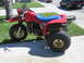 1983 Honda 250 R - This red three-wheeler ATV features a blue seat and gold rims. The engine casing has '200' visible.