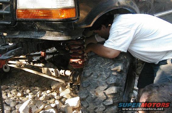 Man looking at the suspension and tire of a large off-road vehicle