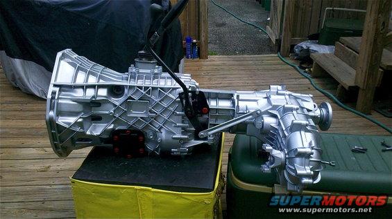 Silver transmission and transfer case assembly on a yellow and black stand next to a green cooler