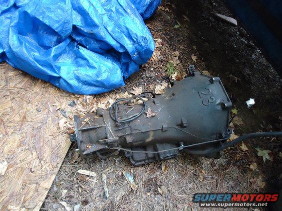 Used transmission with '23' cast into the casing, lying on the ground next to a blue tarp