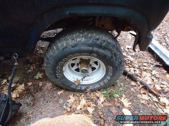 Close-up of a vehicle's front tire and fender, with the wheel showing Firehawk ATX branding. Some debris and leaves are on the ground