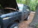 1985 Ford Bronco - This weathered Ford Bronco sits in a wooded area with its hood up, revealing the engine bay.
