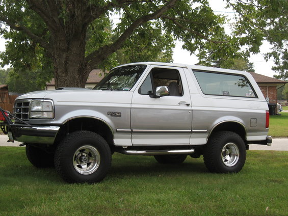 Side view of a two-tone silver and white 1994 Ford Bronco with aftermarket wheels and a brush guard