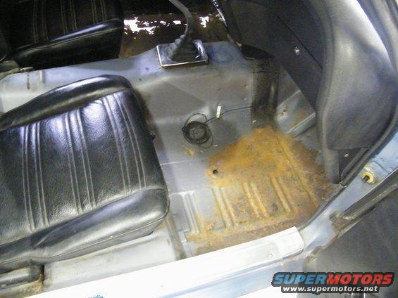 Interior shot of a car's floor showing rusty metal, black seats, and a gear shifter