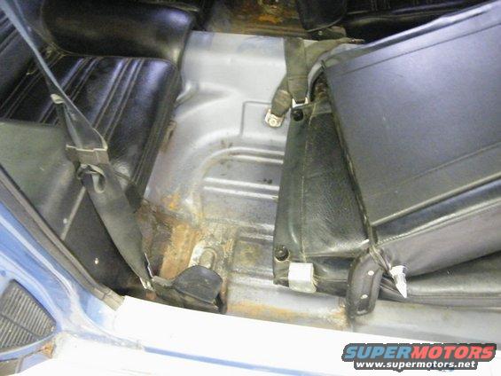 Blue car interior floor with black seats, seatbelts, and rust on the metal floor pan