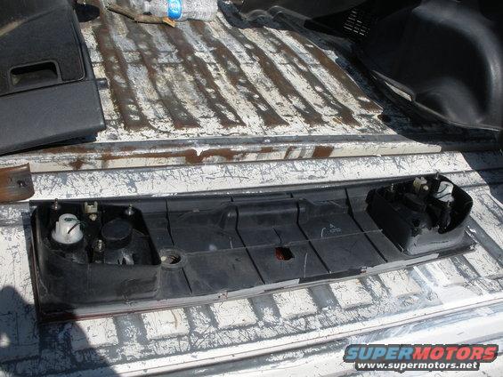 Black plastic tail light assembly with bulbs removed, lying in a truck bed