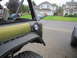 1974 Ford Bronco - Close-up view of the rear quarter panel and taillight assembly on an olive green SUV, with other vehicles visible in the background.