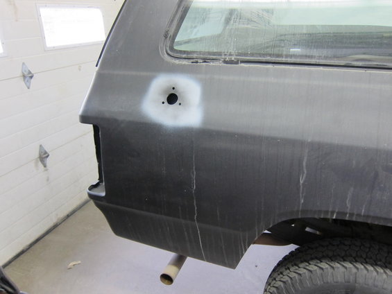 Rear quarter panel of a dark vehicle with a primer spot and three holes