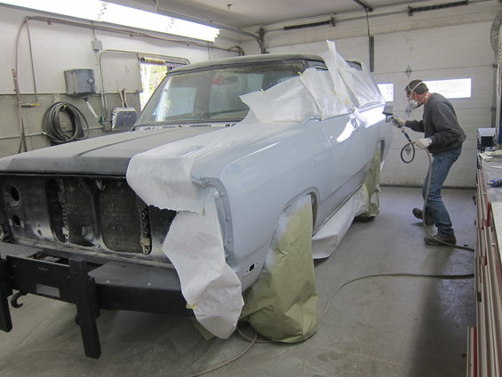 Truck body in a garage, being prepped and painted. A person in a mask is spraying primer