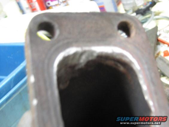 Exhaust manifold flange with two bolt holes and a large opening, showing recent welding work