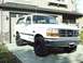 1996 Ford Bronco - White 1996 Ford Bronco parked on a concrete driveway in front of a residential building.