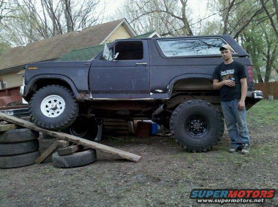 Dark blue Ford Bronco with large tires, lifted, with a man standing next to it