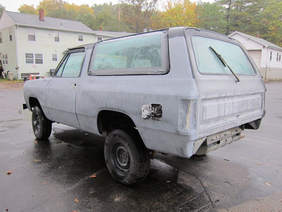 Gray SUV, primer finish, rear 3/4 view, wet asphalt, parked outdoors