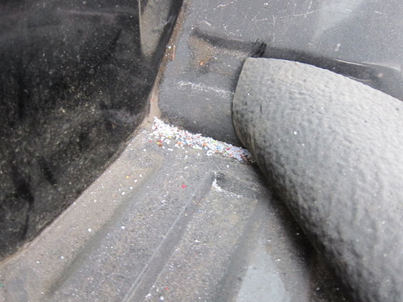 Close-up of a truck bed liner showing dirt and small colorful debris accumulated in a corner
