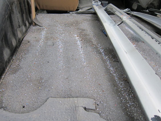 Interior of a truck bed with a textured floor and some debris. A seat is visible in the background