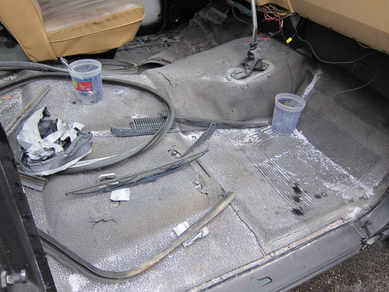Interior of a dirty vehicle with tan seats, scattered debris, and white powder on the floor