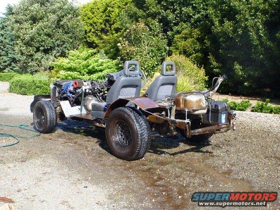 Custom buggy project with exposed engine, two seats, and fuel tank, parked outdoors