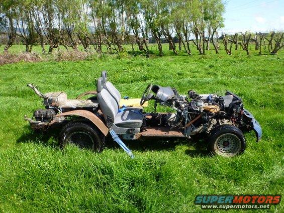 Vehicle chassis with engine exposed, seats, and steering wheel, sitting in a grassy field