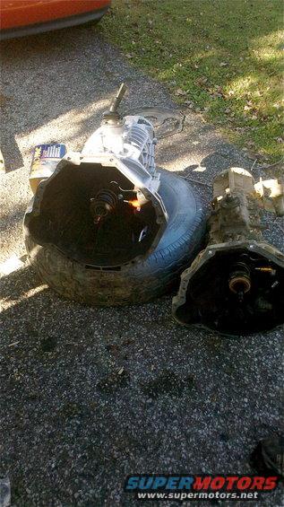Two manual transmissions, one larger than the other, sit on a tire and asphalt