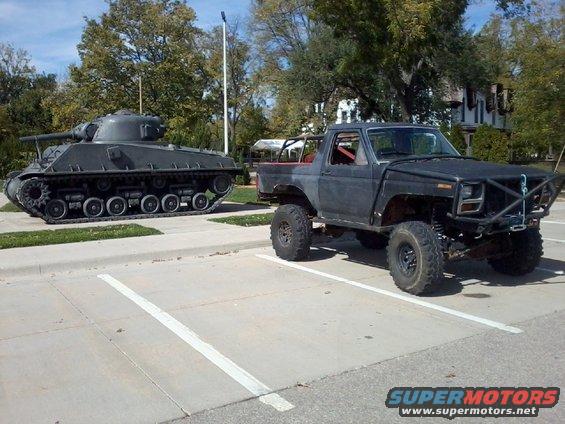 Modified pickup truck parked next to a tank