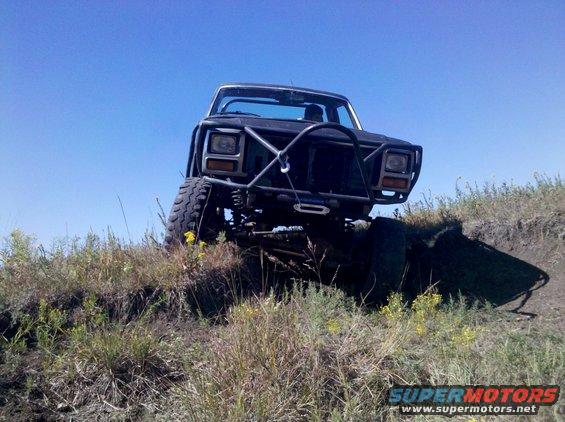 Black off-road SUV with a brush guard and winch climbing a dirt hill under a clear blue sky